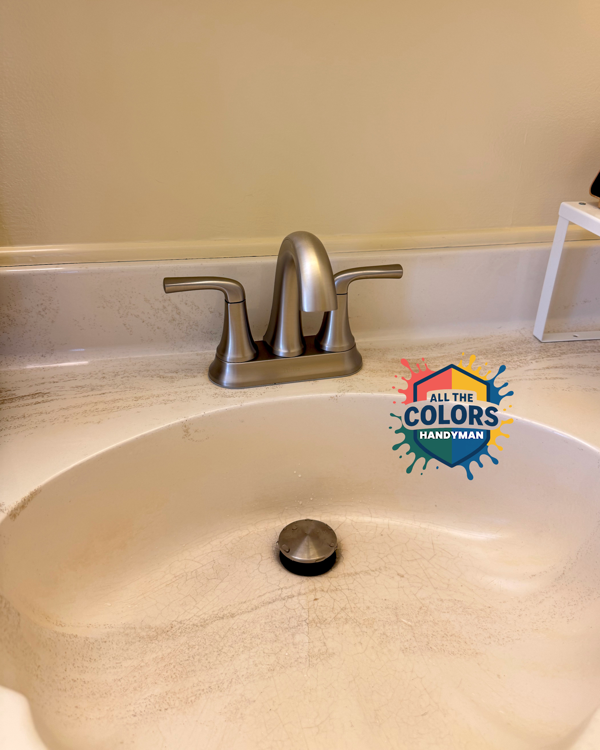 A simple faucet on an off white vanity. The finish is brushed nickel and the forms are restrained. A full-size stopper sits in the drain of the sink.